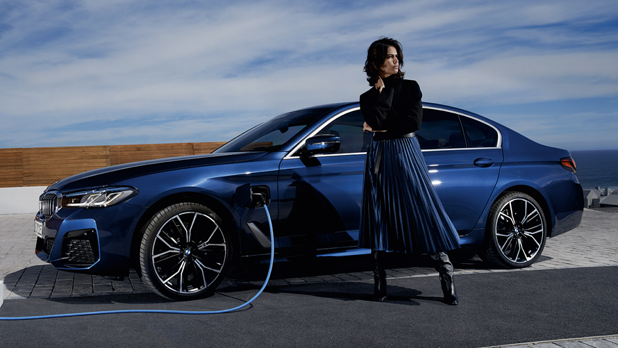 BMW Série 5 Berline Hybride Rechargeable de profil branchée à une borne de recharge BMW Série 5 Berline Hybride Rechargeable de profil branchée à une borne de recharge